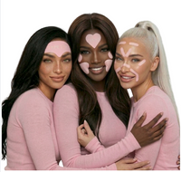 Three diverse women smile and hug while wearing pink TAPETOX anti-aging face tape patches on their foreheads and cheeks.